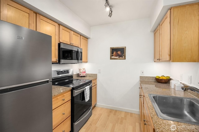 kitchen featuring baseboards, appliances with stainless steel finishes, a sink, light wood-type flooring, and track lighting