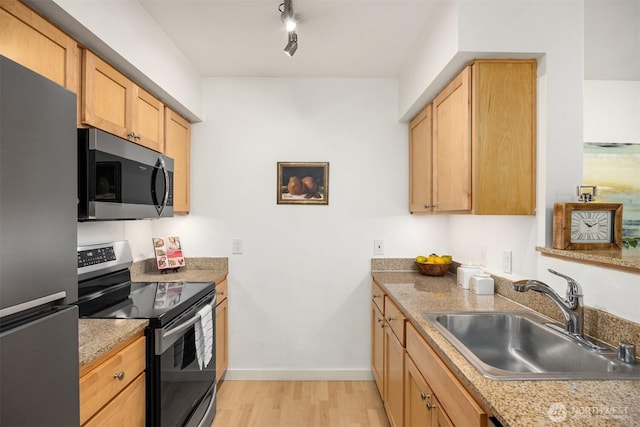 kitchen featuring light wood finished floors, light countertops, appliances with stainless steel finishes, a sink, and baseboards