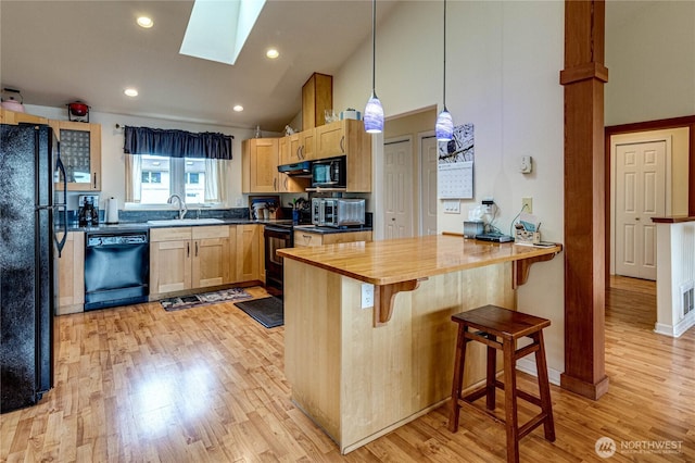 kitchen with a breakfast bar, a skylight, light brown cabinetry, a sink, and black appliances