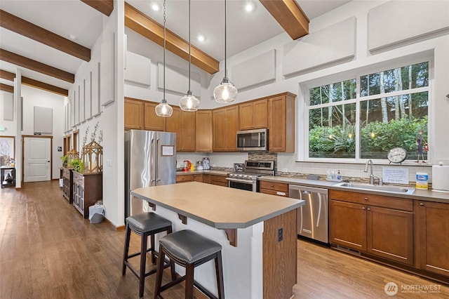 kitchen featuring wood finished floors, a sink, appliances with stainless steel finishes, decorative backsplash, and brown cabinets