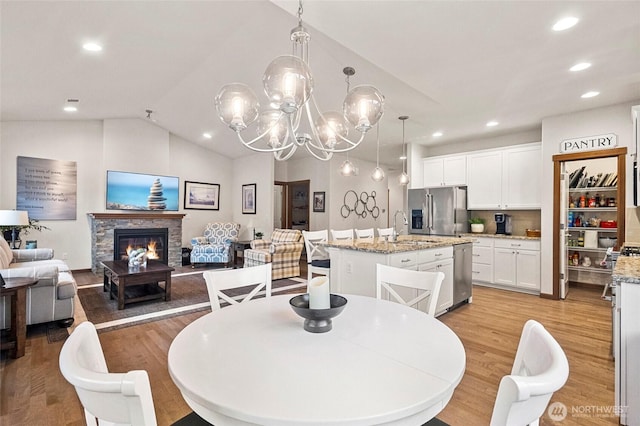 dining area featuring light wood-type flooring, a fireplace, vaulted ceiling, and recessed lighting