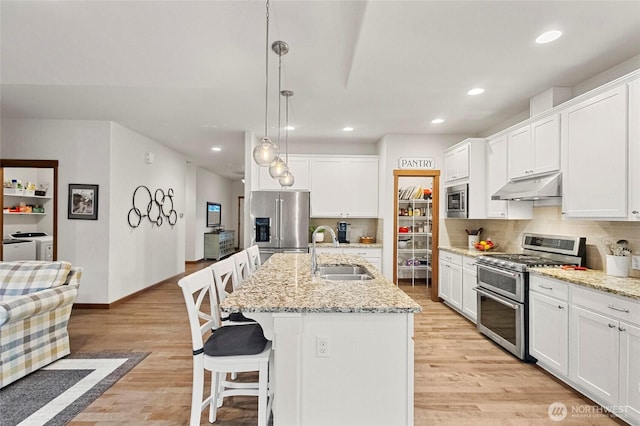 kitchen with under cabinet range hood, stainless steel appliances, separate washer and dryer, a sink, and decorative backsplash