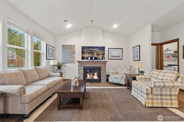 living area with lofted ceiling, visible vents, and a stone fireplace