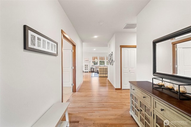 hall featuring light wood-type flooring, visible vents, and baseboards