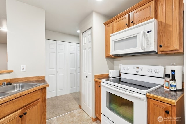 kitchen with white appliances, brown cabinets, a sink, and light carpet