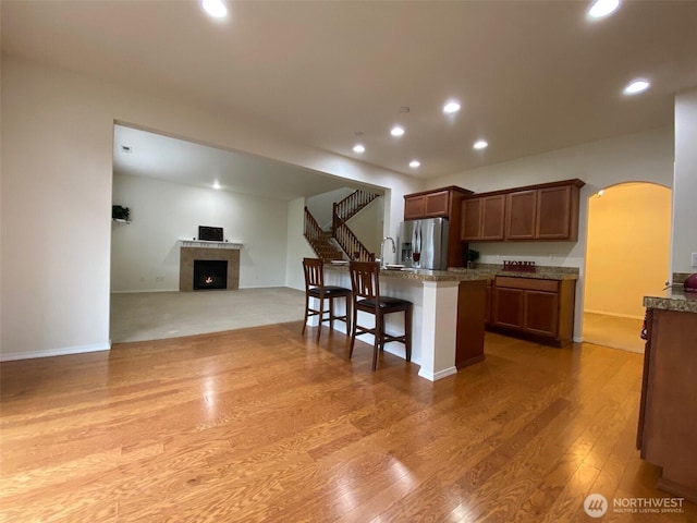 kitchen featuring arched walkways, a kitchen island with sink, a kitchen breakfast bar, open floor plan, and stainless steel fridge