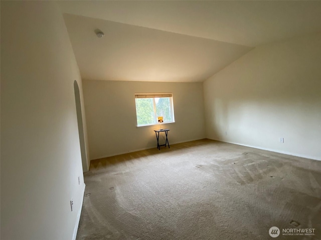 spare room featuring lofted ceiling, carpet floors, and arched walkways