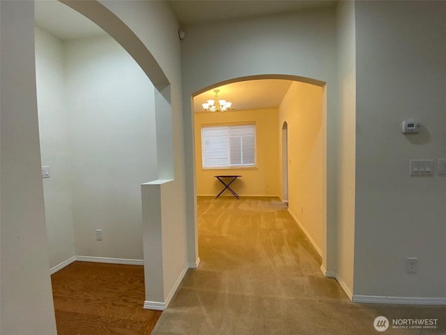 hallway featuring baseboards, arched walkways, and light colored carpet