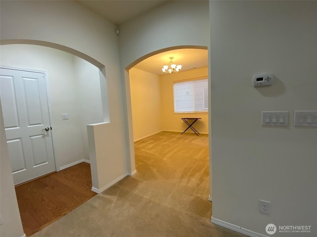 hallway with carpet flooring, baseboards, and an inviting chandelier