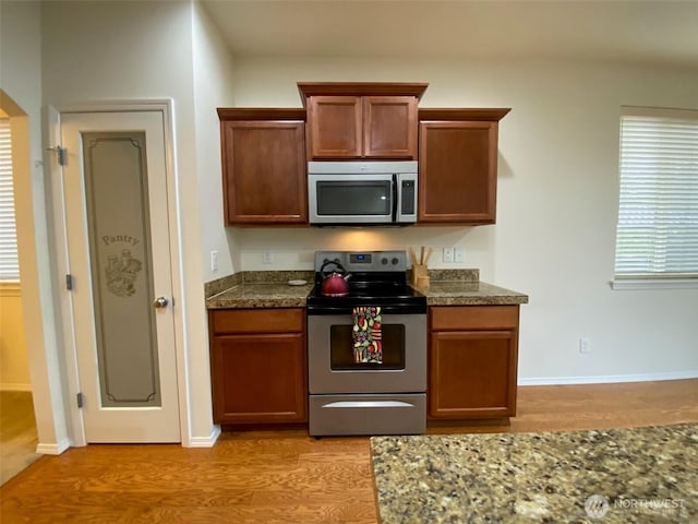 kitchen with stainless steel appliances, brown cabinetry, light wood-style floors, and dark stone countertops