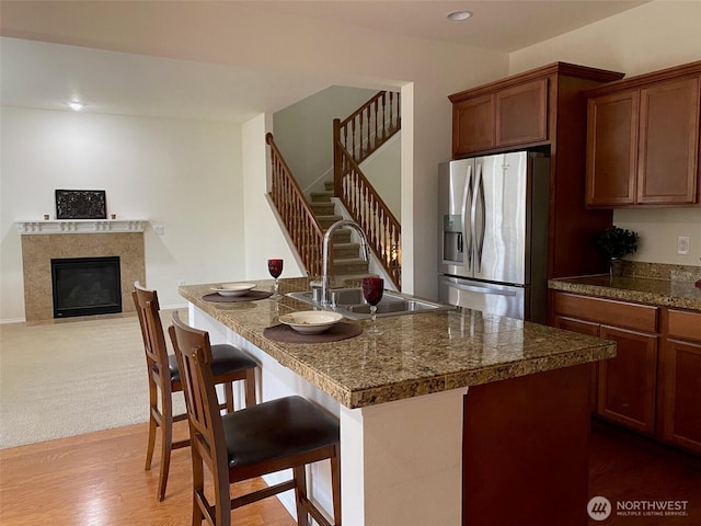 kitchen with a center island with sink, a glass covered fireplace, a kitchen bar, stainless steel refrigerator with ice dispenser, and a sink