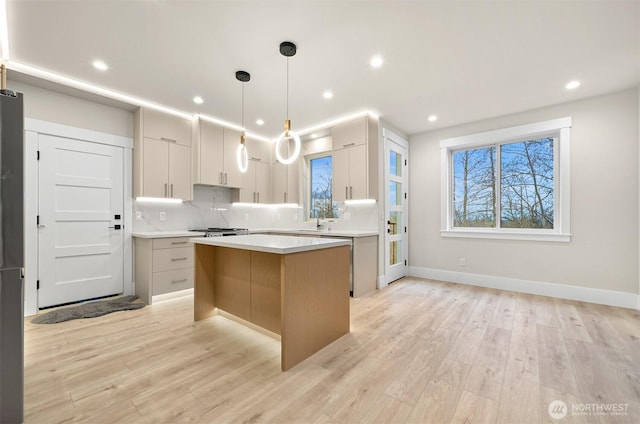 kitchen featuring a kitchen island, light countertops, decorative backsplash, modern cabinets, and decorative light fixtures