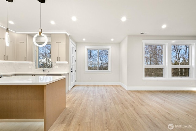 kitchen with decorative backsplash, light wood-style flooring, hanging light fixtures, light countertops, and white cabinetry