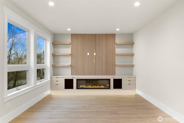 unfurnished living room featuring light wood finished floors, baseboards, a glass covered fireplace, and recessed lighting