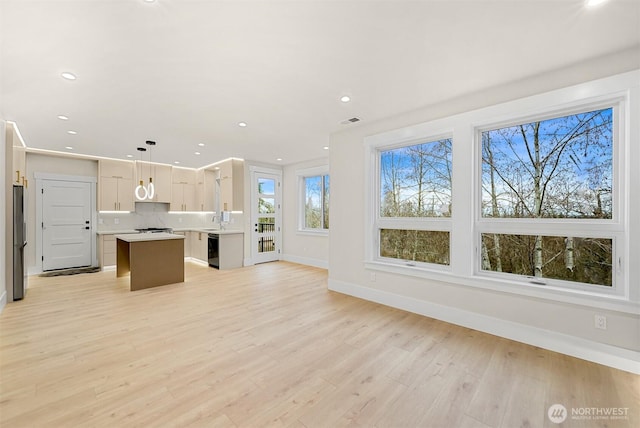 kitchen with open floor plan, freestanding refrigerator, hanging light fixtures, a center island, and light countertops