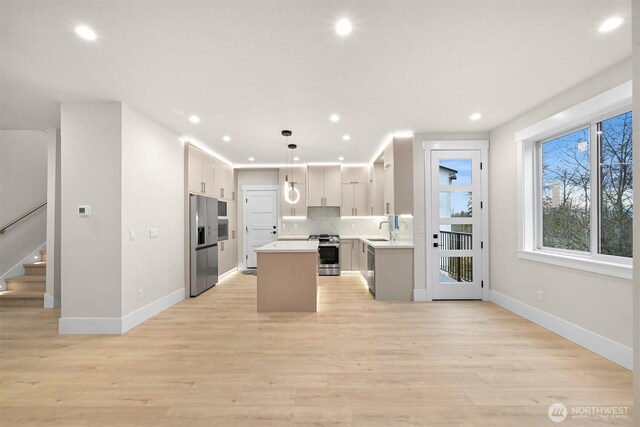 kitchen with a kitchen island, appliances with stainless steel finishes, decorative light fixtures, light countertops, and a sink