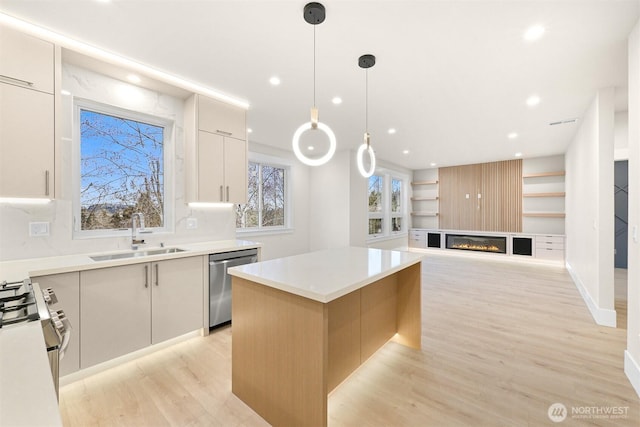 kitchen featuring light countertops, hanging light fixtures, appliances with stainless steel finishes, a sink, and a kitchen island