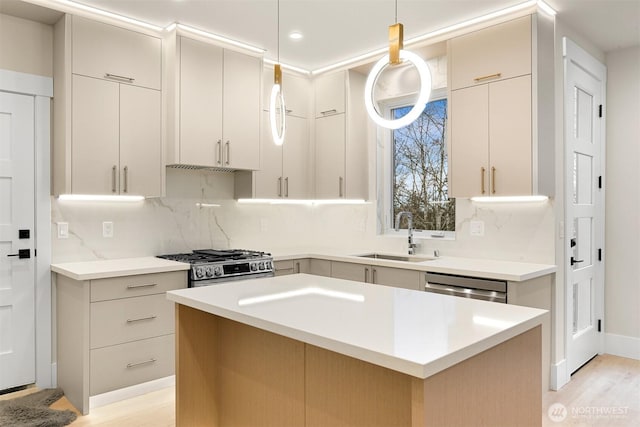 kitchen with a kitchen island, a sink, hanging light fixtures, appliances with stainless steel finishes, and light countertops