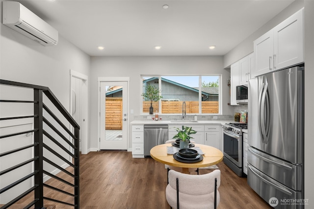 kitchen featuring light countertops, appliances with stainless steel finishes, an AC wall unit, white cabinets, and a sink