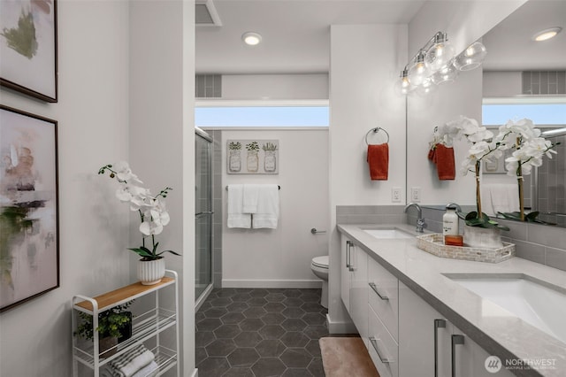 bathroom with a stall shower, a sink, toilet, and double vanity