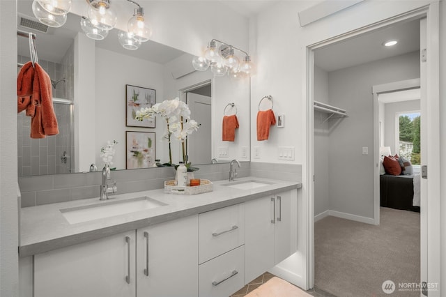 full bath with double vanity, a sink, a walk in closet, and baseboards