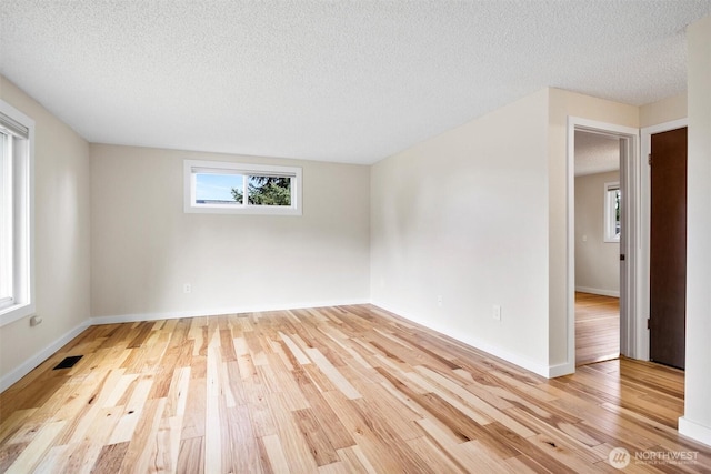 empty room with a textured ceiling, light wood-type flooring, visible vents, and baseboards