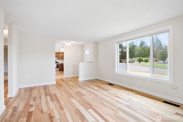 unfurnished living room featuring light wood-type flooring, visible vents, a textured ceiling, and baseboards