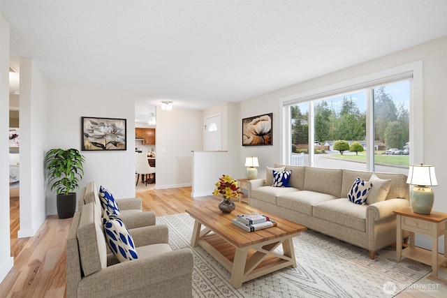 living room featuring baseboards, a textured ceiling, and light wood finished floors