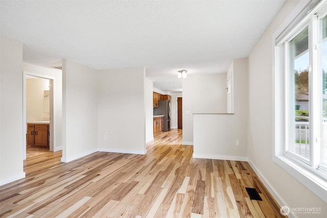 spare room featuring light wood finished floors, visible vents, and baseboards