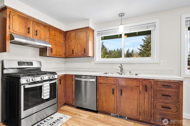 kitchen with light wood-style flooring, under cabinet range hood, a sink, appliances with stainless steel finishes, and brown cabinets