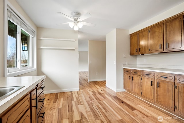 kitchen with light countertops, brown cabinetry, light wood-style flooring, and baseboards