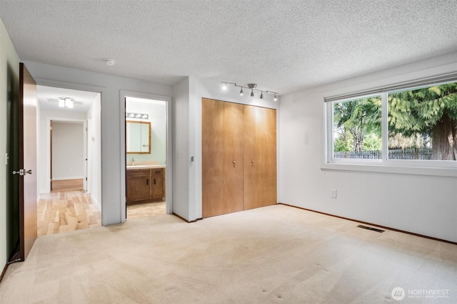 unfurnished bedroom with a textured ceiling, a closet, visible vents, and light colored carpet