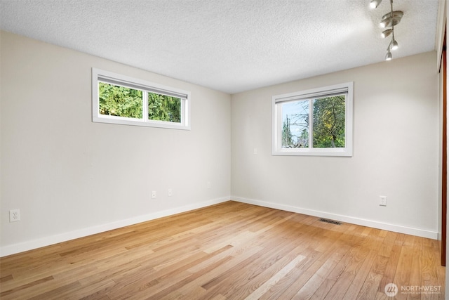 empty room featuring baseboards, plenty of natural light, a textured ceiling, and light wood finished floors