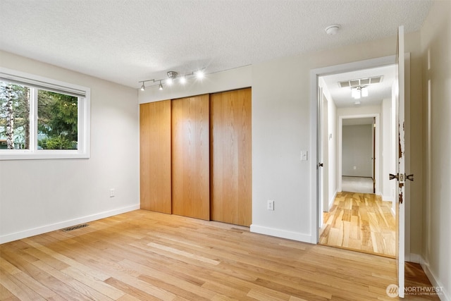 unfurnished bedroom featuring a textured ceiling, a closet, light wood-type flooring, and visible vents