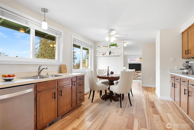 kitchen with a sink, stainless steel dishwasher, light wood finished floors, brown cabinetry, and decorative light fixtures