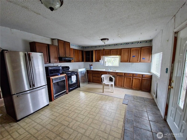 kitchen featuring brown cabinetry, under cabinet range hood, light countertops, black appliances, and a sink