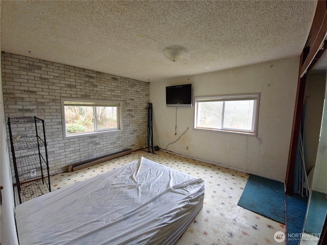 unfurnished bedroom featuring light floors, brick wall, a baseboard heating unit, and a textured ceiling