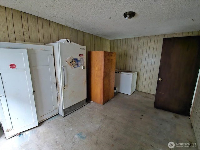 interior space featuring wooden walls, a textured ceiling, and freestanding refrigerator