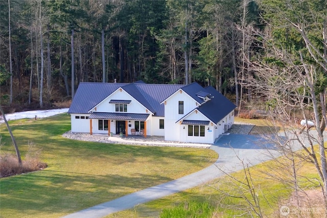 modern farmhouse with a standing seam roof, metal roof, a front lawn, and a wooded view