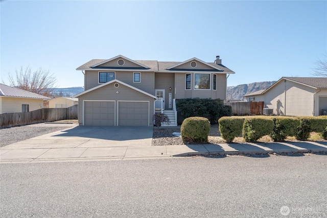 bi-level home featuring a garage, concrete driveway, a chimney, and fence