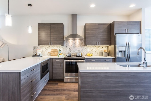 kitchen featuring appliances with stainless steel finishes, light countertops, wall chimney range hood, pendant lighting, and a sink