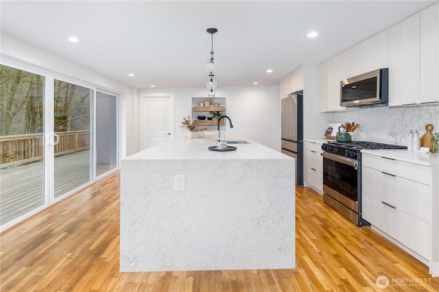 kitchen with appliances with stainless steel finishes, pendant lighting, white cabinetry, modern cabinets, and light wood-type flooring