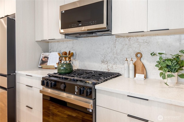 kitchen featuring stainless steel microwave, tasteful backsplash, freestanding refrigerator, range with gas cooktop, and light countertops