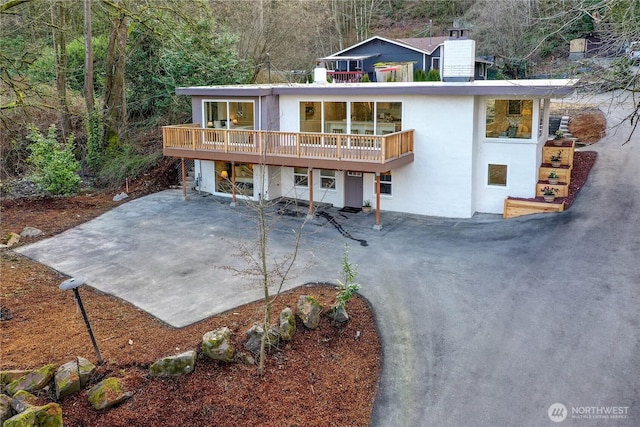 rear view of house with a wooden deck, a patio area, driveway, and stucco siding