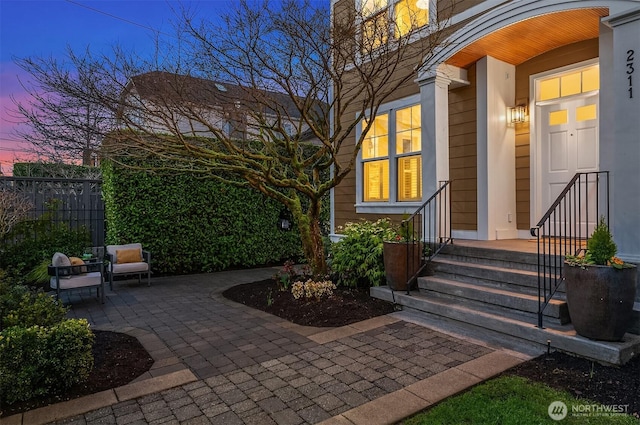 exterior entry at dusk featuring fence and a patio