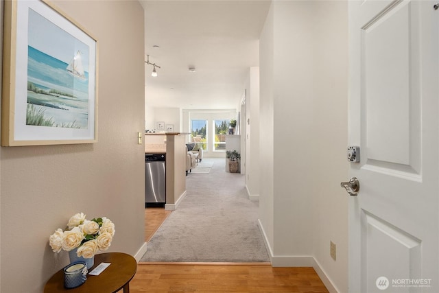 corridor featuring rail lighting, light wood-style flooring, and baseboards