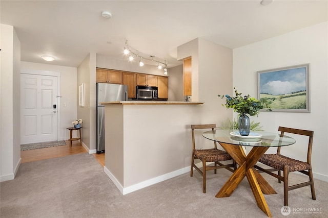 kitchen with appliances with stainless steel finishes, brown cabinets, light carpet, and baseboards