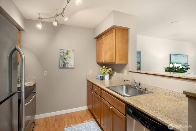 kitchen featuring baseboards, light wood-style flooring, appliances with stainless steel finishes, brown cabinets, and a sink