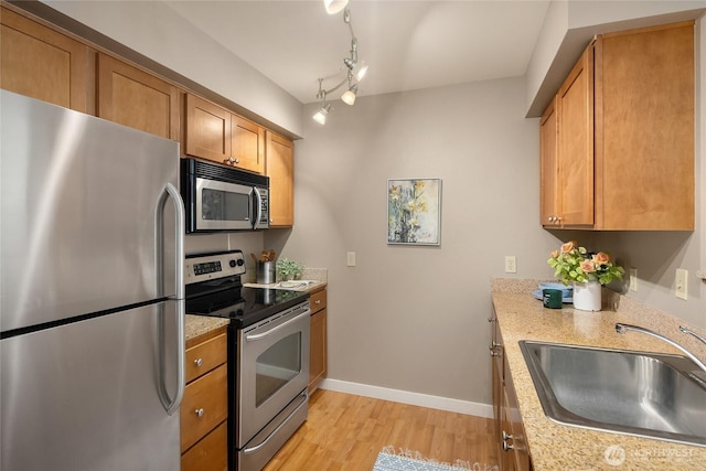 kitchen with a sink, baseboards, appliances with stainless steel finishes, light wood finished floors, and brown cabinetry