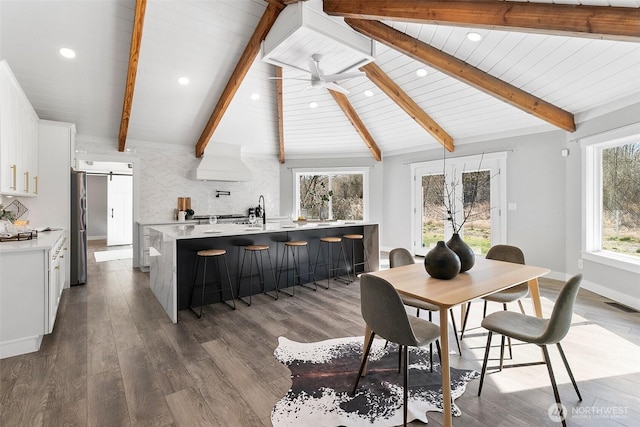 dining area with lofted ceiling with beams, a barn door, dark wood-style flooring, visible vents, and a ceiling fan